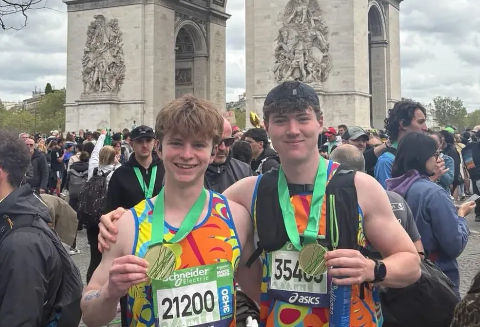Two student runners with their Paris Marathon medals in front of the Arc de Triomphe