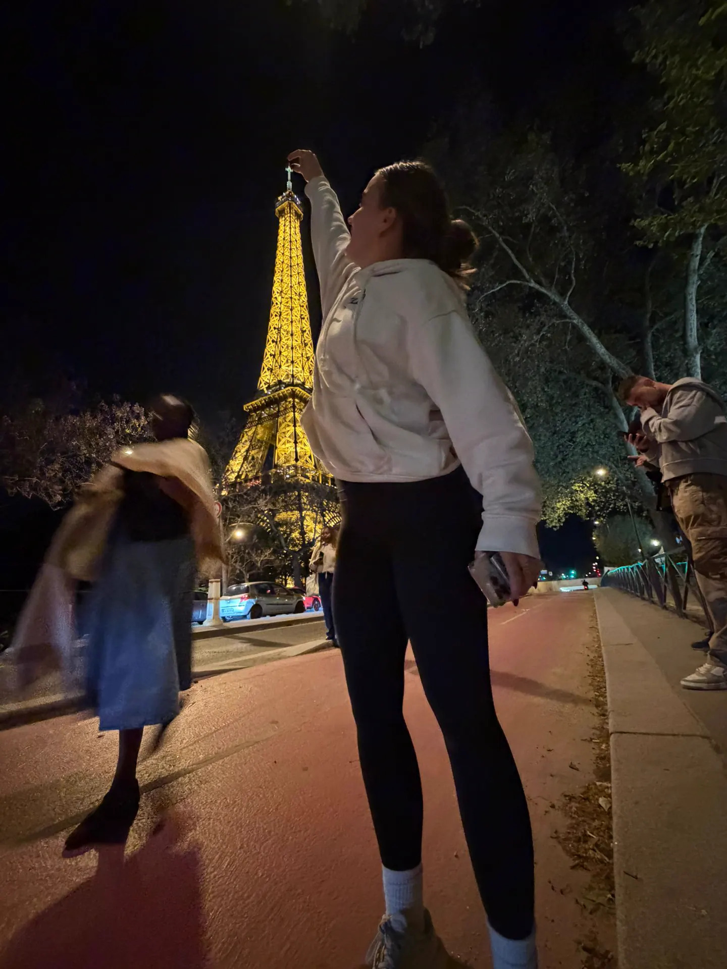 Runner posing for a perspective trick photo pinching the top of the Eiffel Tower as it sparkles at night in Paris.