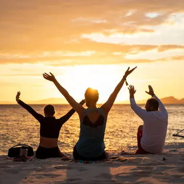 Three friends with arms raised watching the sunset from the sand on the SYB Philippines trip