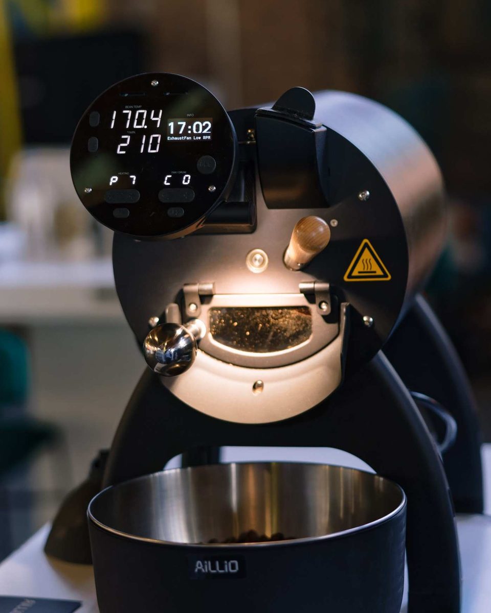 An Aillio coffee roaster glowing as it roasts, with its digital display lit up