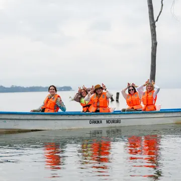 Crew in orange life jackets waving from a boat on calm water in Kenya