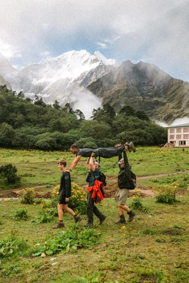 Trekkers and a porter crossing a green alpine meadow below the snow line on the way into the high Khumbu