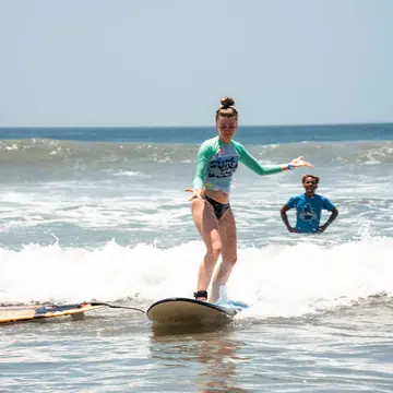 Standing up on a small wave with another surfer watching from the water on the SYB Nicaragua Surf Camp trip