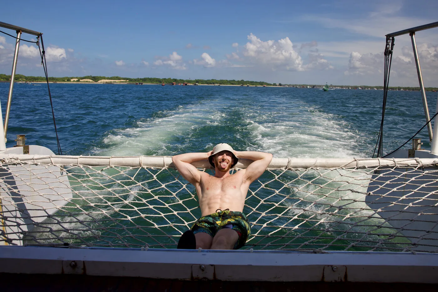 A traveler relaxing on the boat net with the wake behind, on the SYB Bali trip