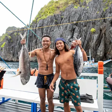 Two guys holding up big fish on the boat deck in front of limestone cliffs on the SYB Philippines trip