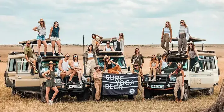 The whole crew posing on and around safari jeeps with the Surf Yoga Beer flag in Kenya