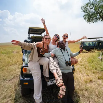 Friends posing with arms out on the front of a safari jeep on the SYB Kenya trip