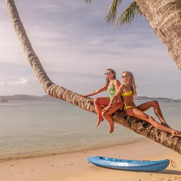 Two friends sitting on a leaning palm tree over the beach on the SYB Philippines trip