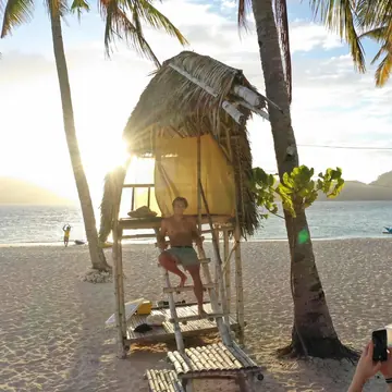 Small thatched hut on stilts between palm trees on the beach in the late sun on the SYB Philippines trip