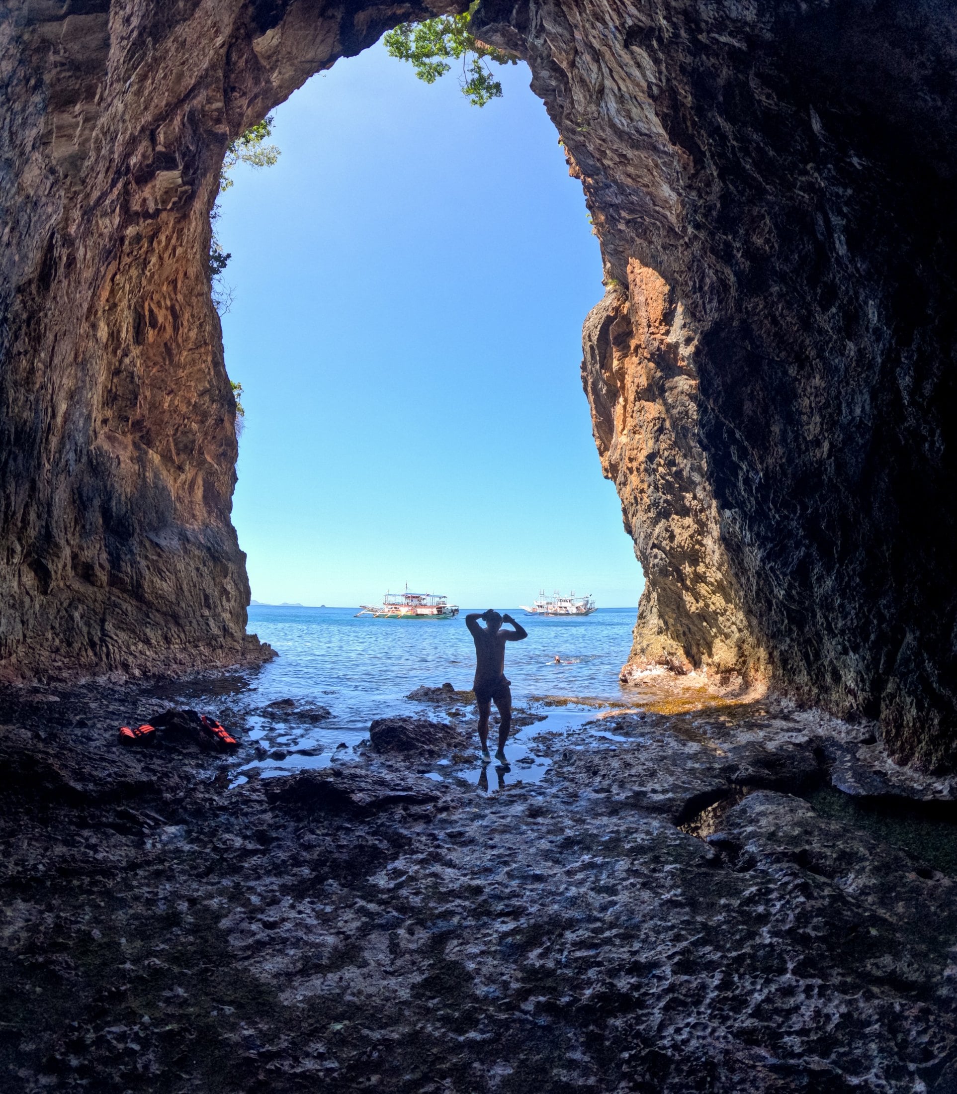 SurfYogaBeer guest standing in a sea cave arch looking out at the boats in Palawan