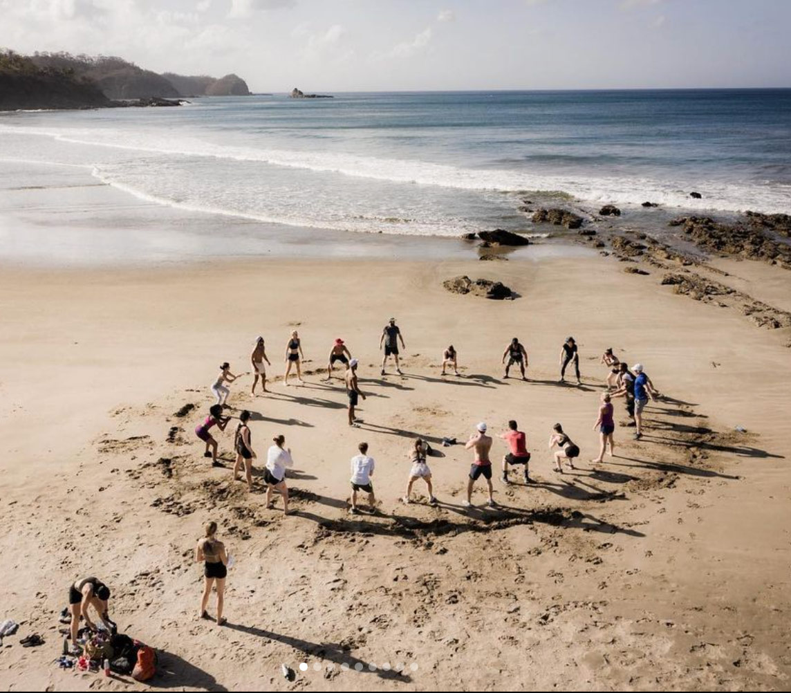A group workout in a circle on the beach at Playa Maderas, seen from above