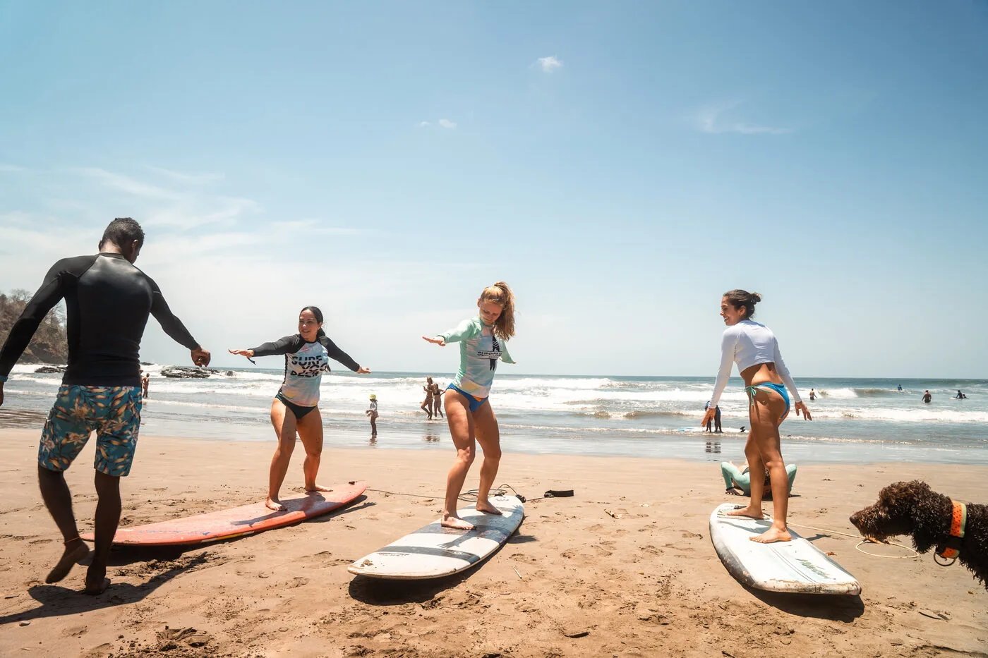 A surf instructor teaching three beginners on the sand at Playa Maderas, Nicaragua