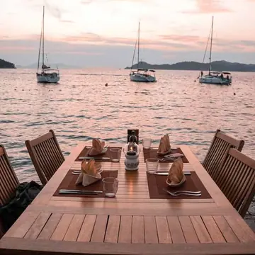 Dinner table set by the water with sailboats at sunset on the SYB Croatia trip