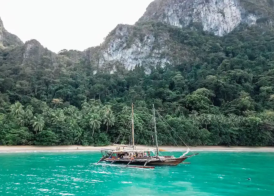 Traditional Filipino paraw outrigger sailing past the Palawan cliffs