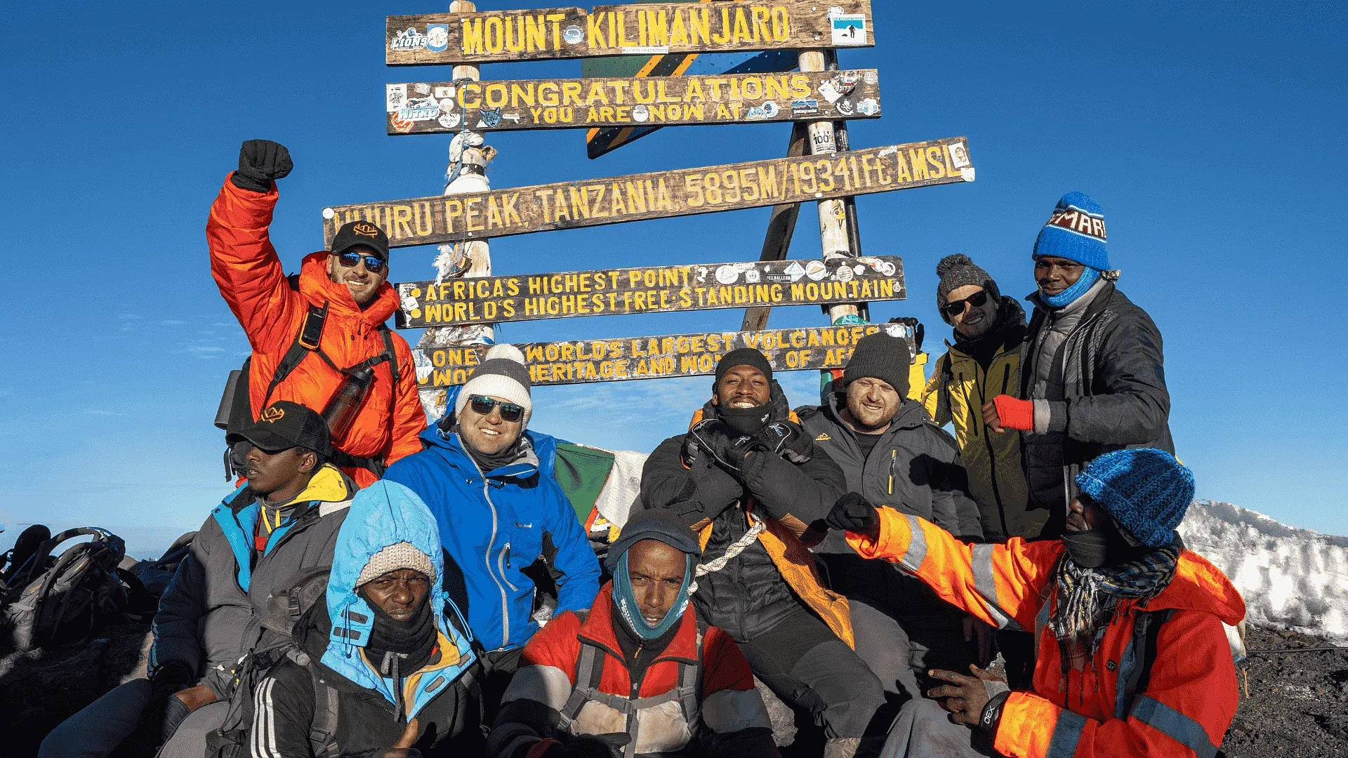 A group celebrating at the Kilimanjaro summit sign