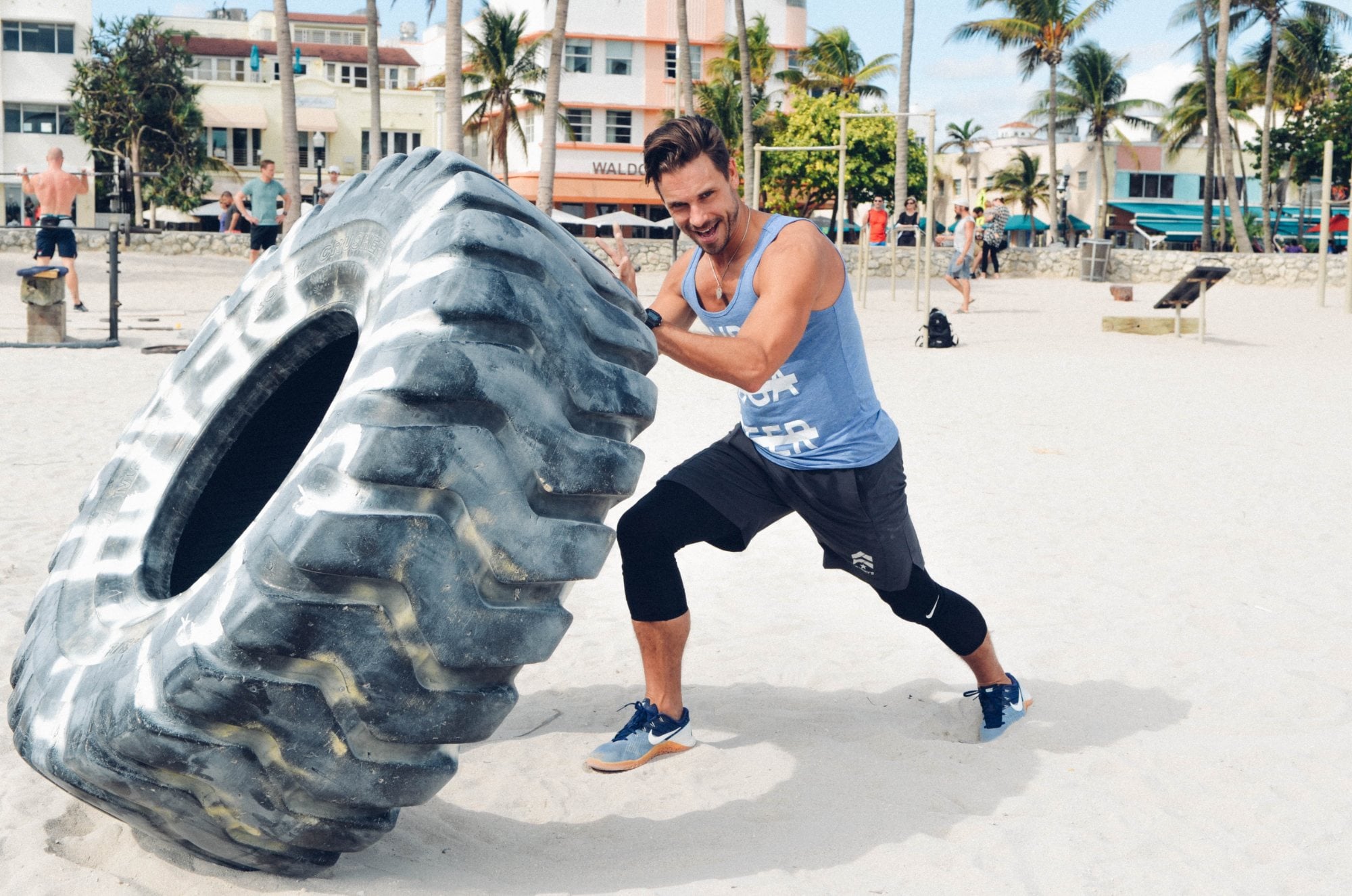 SYB crew member flipping a tire on Miami Beach in a cross-out tank