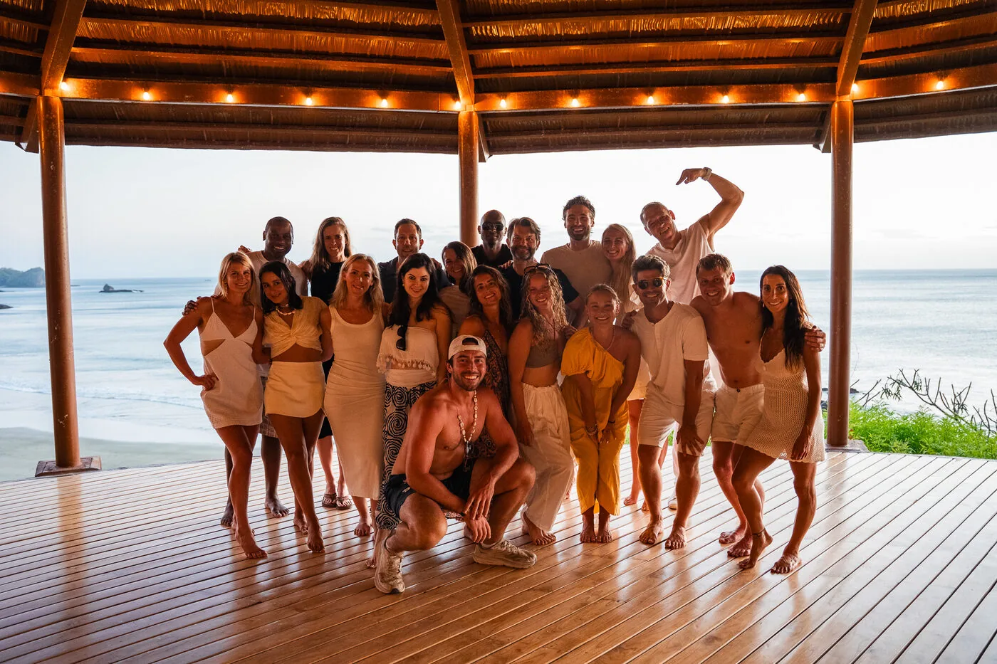 An SYB crew posing together on a deck under a thatched roof with string lights, the Pacific behind them, in Nicaragua