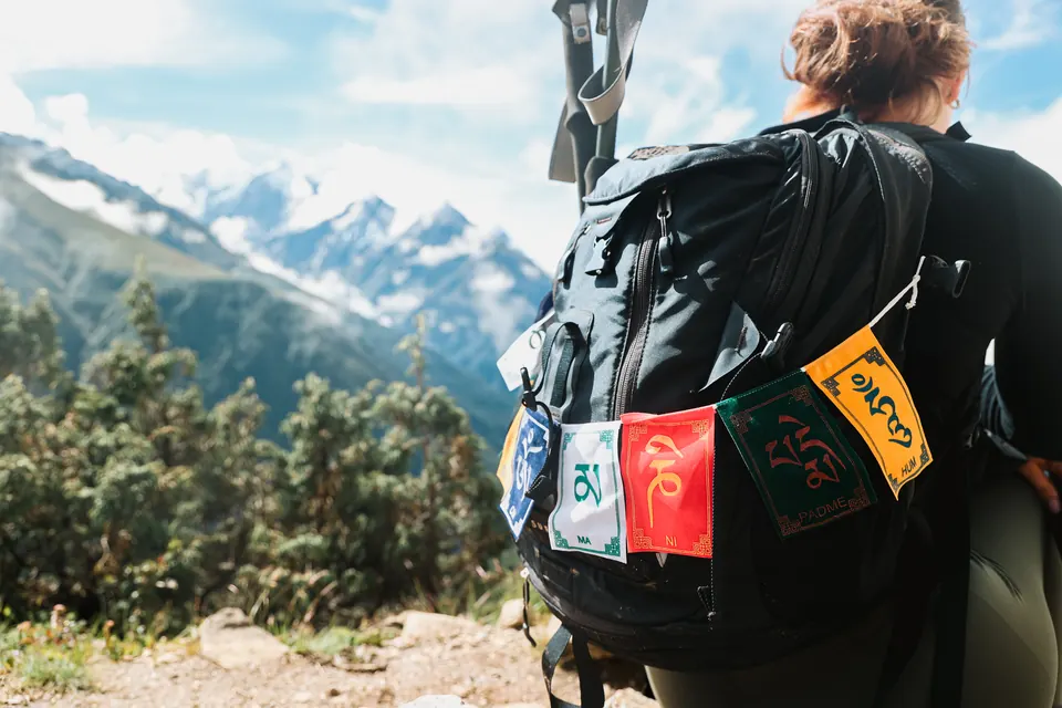 Prayer flags tied to a trekker's pack above Namche Bazaar with snow peaks behind