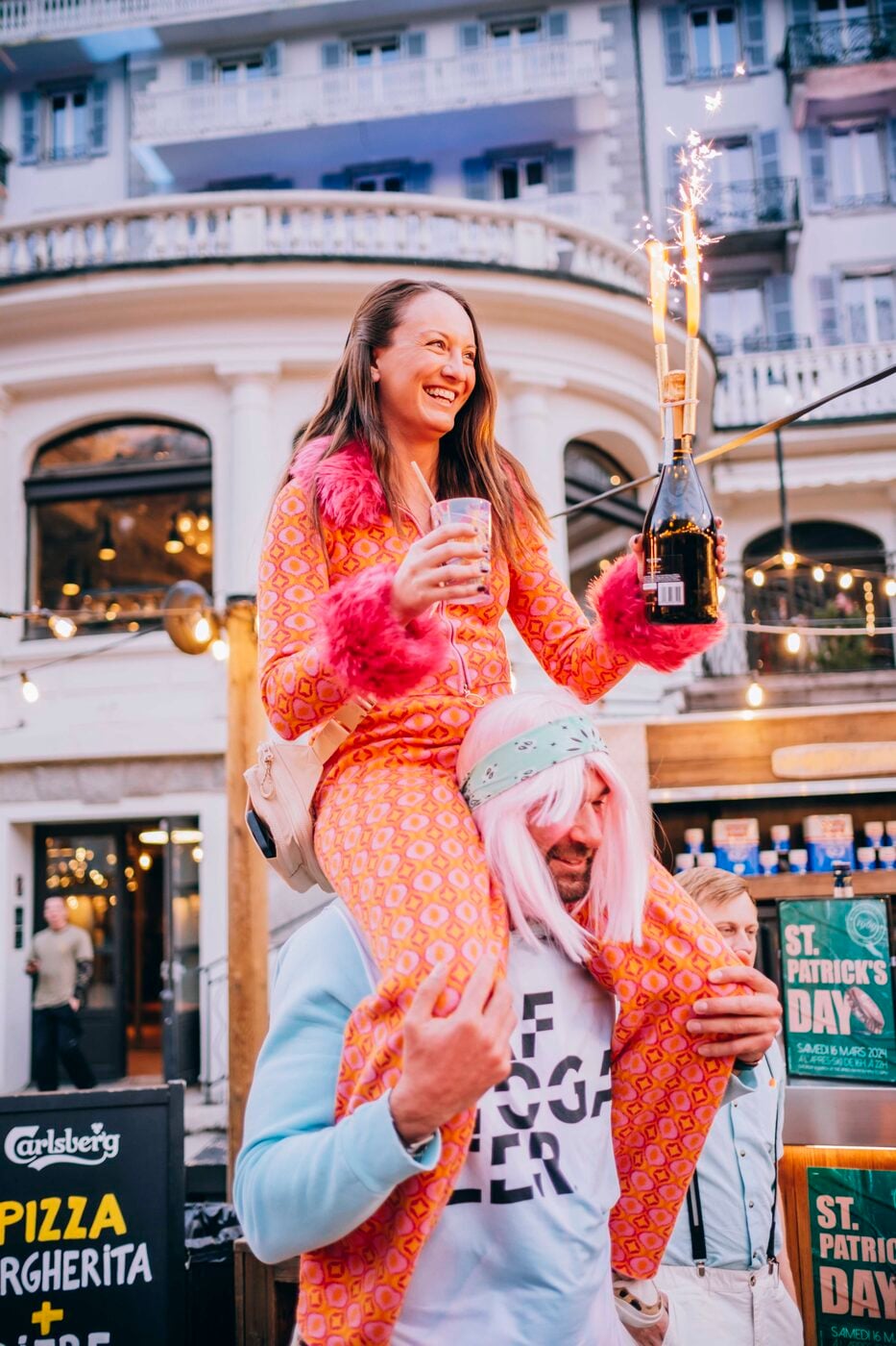 A traveler on a friend's shoulders holding a drink in Chamonix town