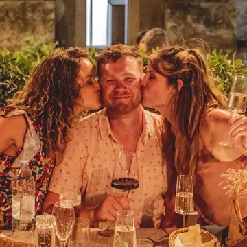 Two friends kissing a third on the cheeks at the dinner table on the SYB Croatia trip