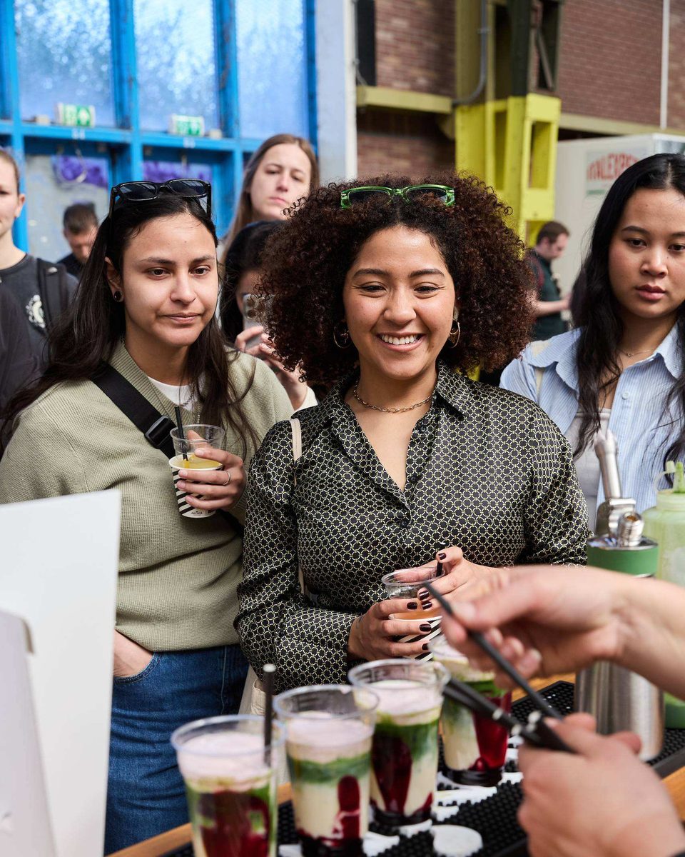 Smiling visitors pick up layered drinks from a tray at the MONIN bar