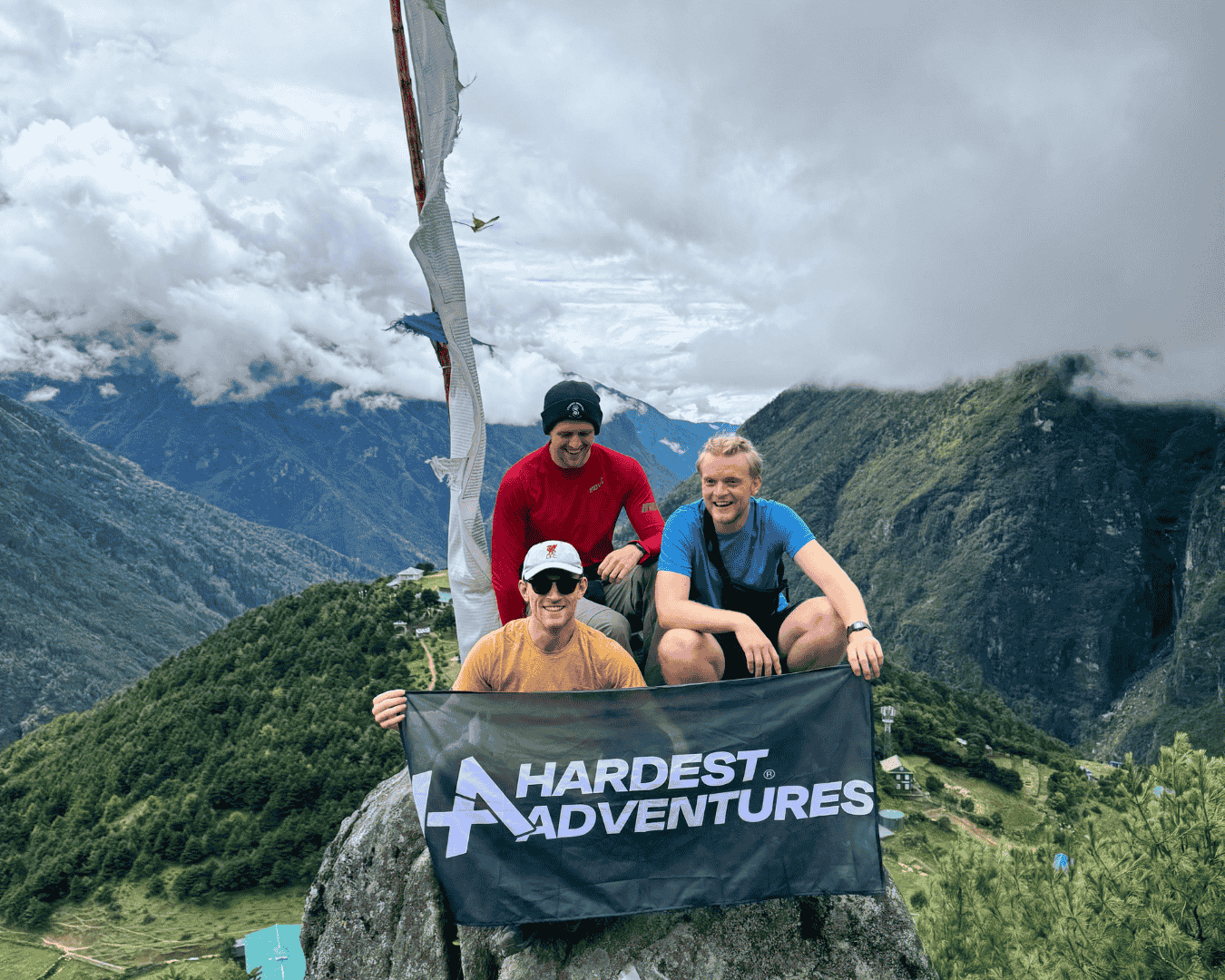 Group of male hikers sitting on a rock holding a Hardest Adventures banner with a view of the Himalayas in the background on their way to everest base camp.