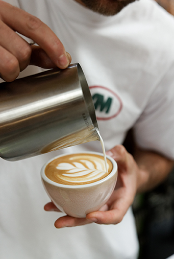 Gros plan sur un barista tra&ccedil;ant une rosetta en latte art