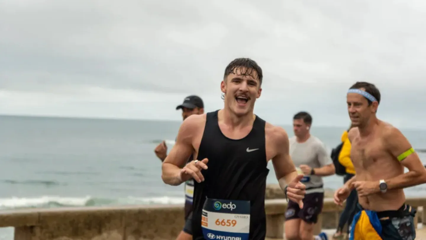 Grinning Hardest Adventures runner leading a group of racers along a seafront road on marathon race day.