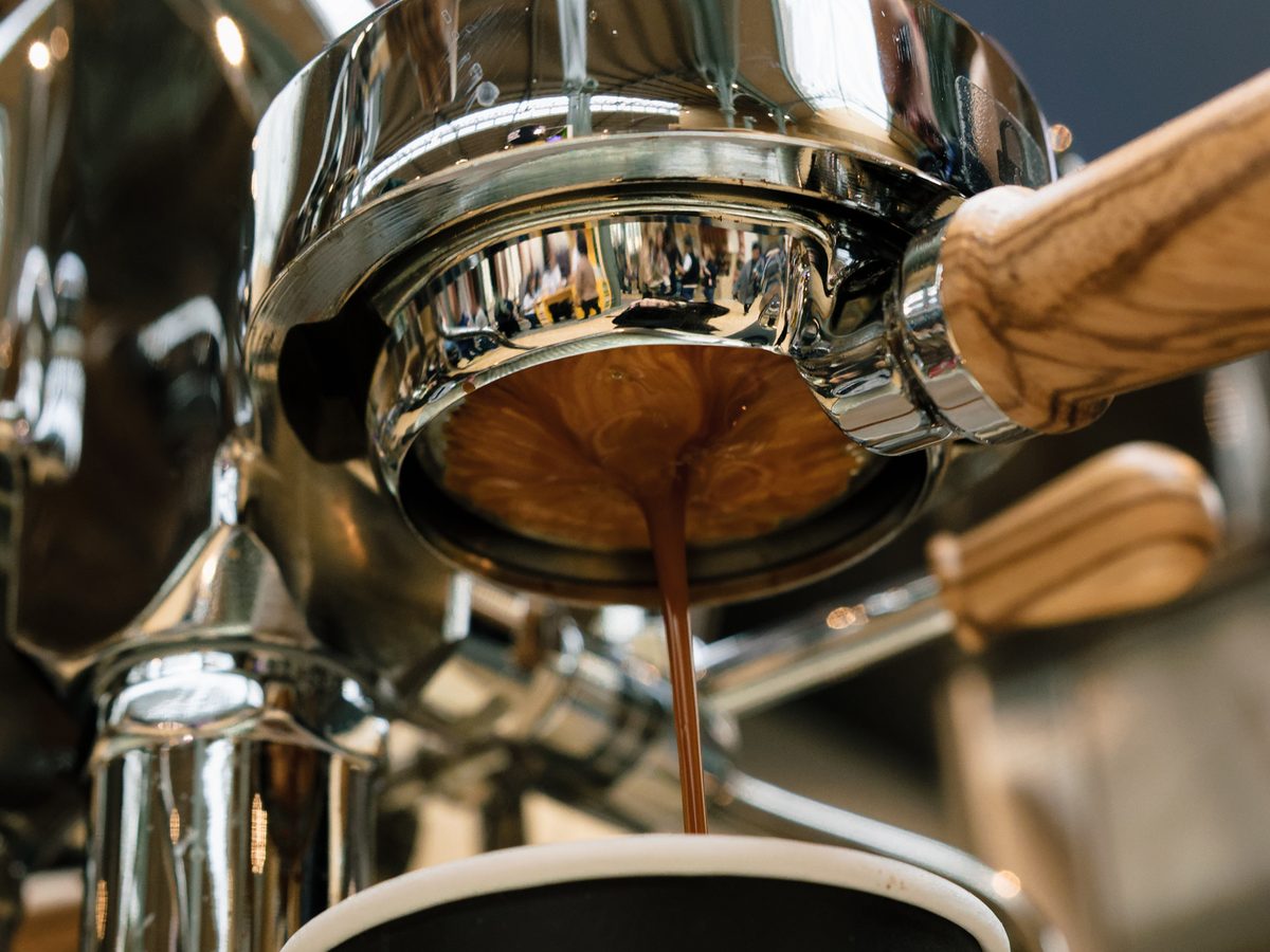 Espresso streams from a portafilter on a polished espresso machine