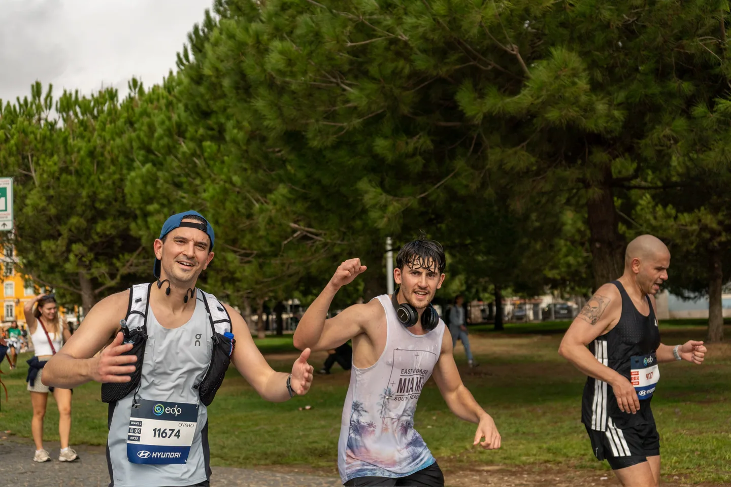 Two runners laughing and joking for the camera mid-race on a tree-lined marathon route.