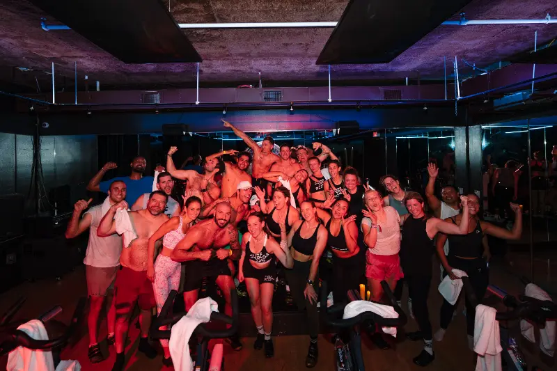 The whole cycling class on the bikes, arms up