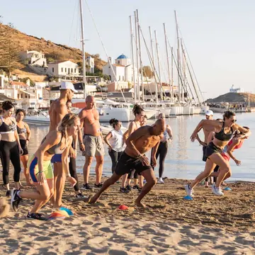 Group workout on the sand beside a harbour full of sailboats on the SYB Greece trip