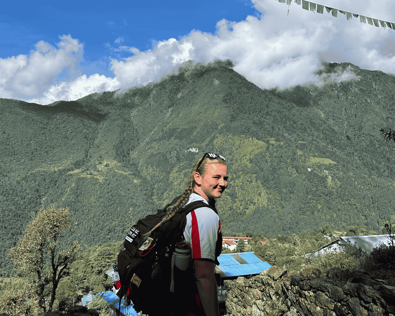 Picture of hiker turning back and smiling with the Himalayas as their backdrop on their way to Everest base camp with hardest adventures.