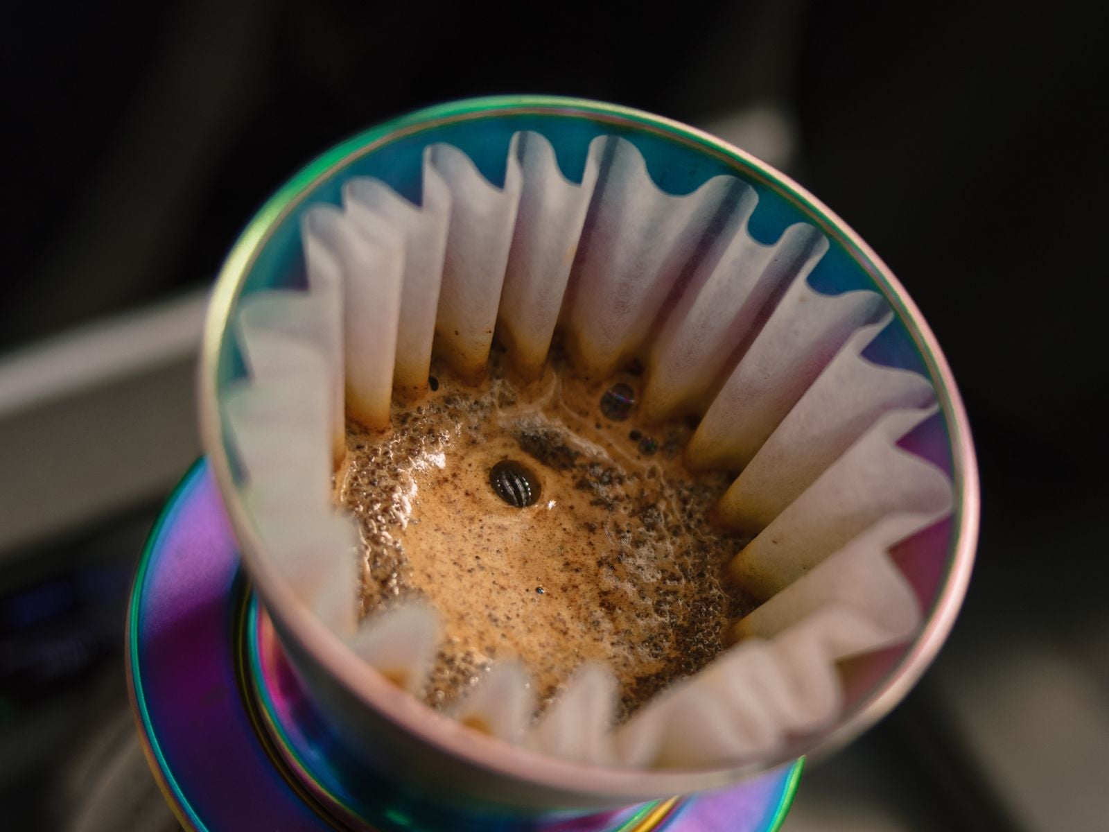 Coffee blooming in a paper filter inside an iridescent pour-over dripper