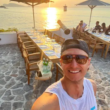 Selfie beside a long table set for dinner on a terrace at sunset on the SYB Greece trip