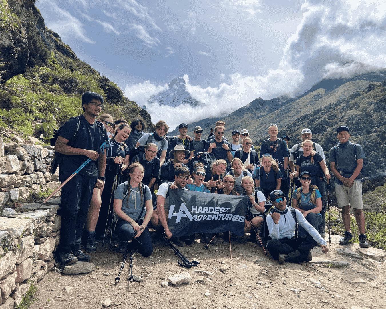 Group of hikers posing with a Hardest Adventures banner with the first view of Ama Dablam in the background of their affordable trek to Everest Base Camp.