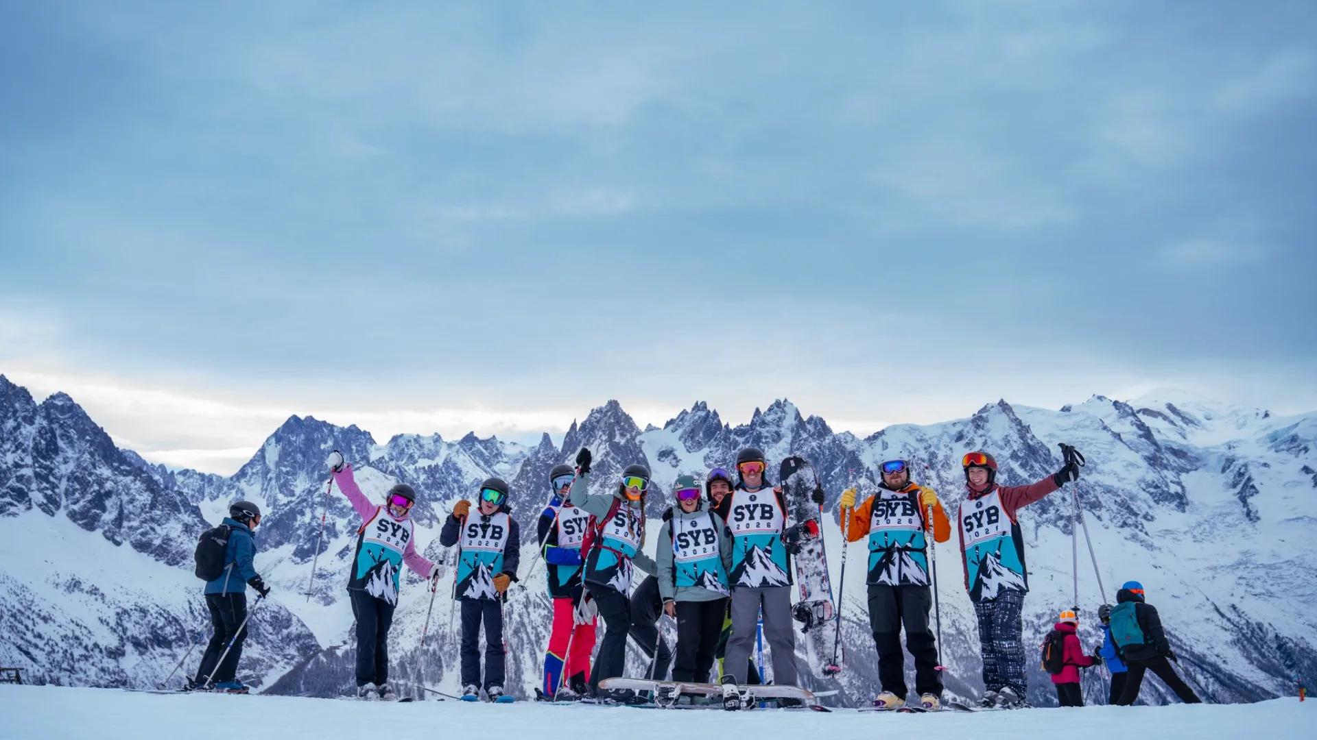 SurfYogaBeer crew in SYB bibs lined up on skis under the Mont Blanc massif