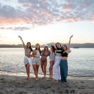 Five friends with their arms up on the beach at sunset on the SYB Philippines trip
