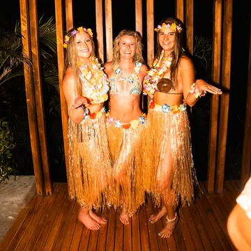 Three friends in grass skirts and flower crowns for a theme night on the SYB Nicaragua Surf Camp trip