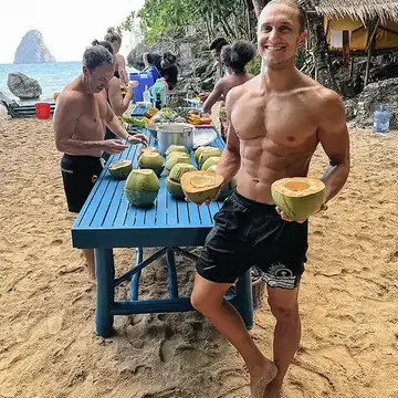Holding a cut coconut beside a table of fresh coconuts on the beach on the SYB Philippines trip