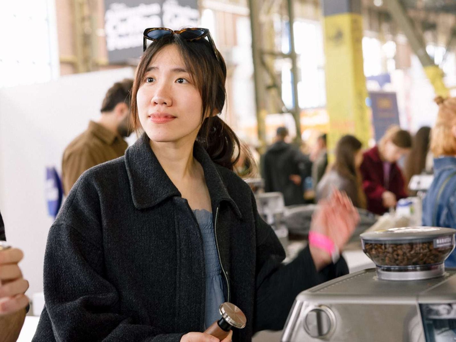A visitor holds a tamper beside an espresso machine during a Coffee School workshop