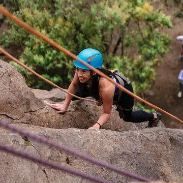 Climber in a blue helmet scrambling up a rock face with ropes on the SYB Kenya trip