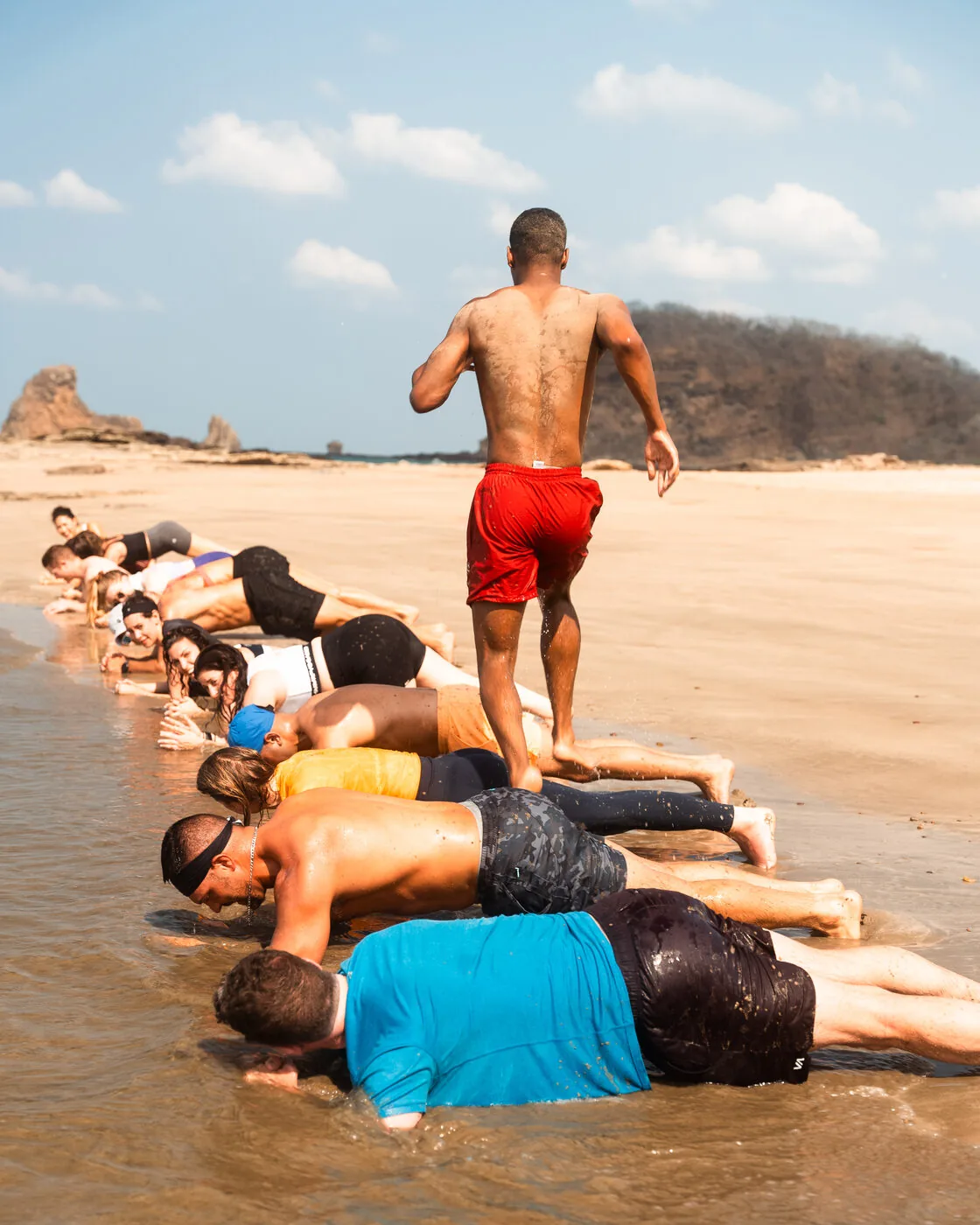 A morning workout on the sand at Playa Maderas with a coach standing over a line of people holding a plank