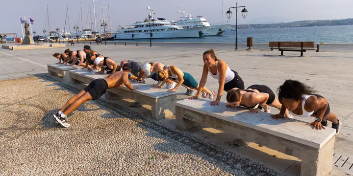 Group push ups on the stone benches of a harbour promenade on the SYB Greece trip