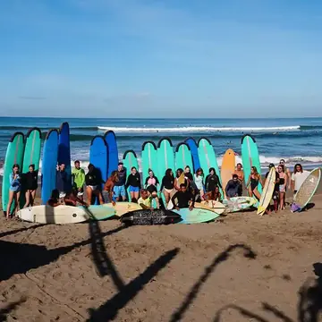 The group lined up with their surfboards on a dark sand beach on the SYB Bali trip
