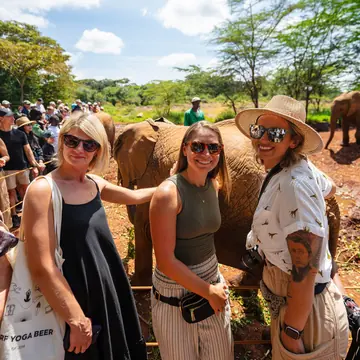 Three friends smiling in front of a herd of elephants on the SYB Kenya trip