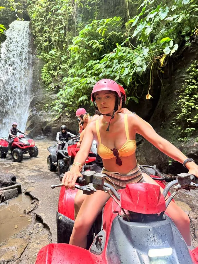 A traveler on an ATV in front of a jungle waterfall near Ubud, Bali