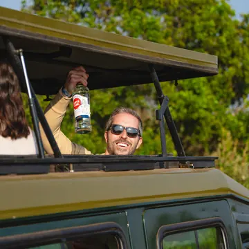 Guest standing out of the jeep roof with a drink on the SYB Kenya trip