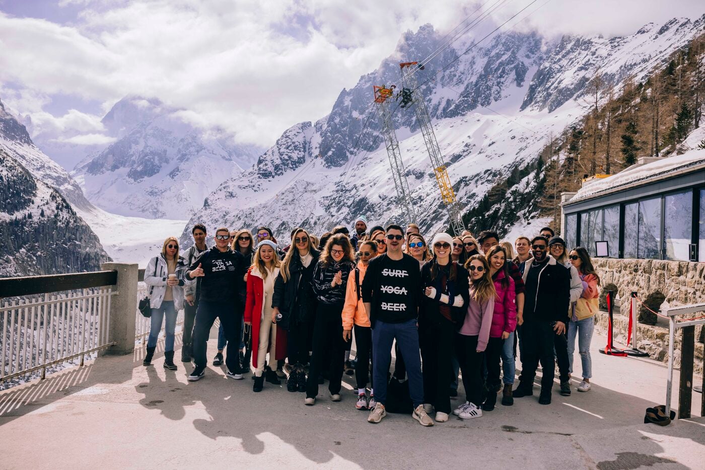 A big SYB ski crew posing together on a snowy terrace with the mountains behind them