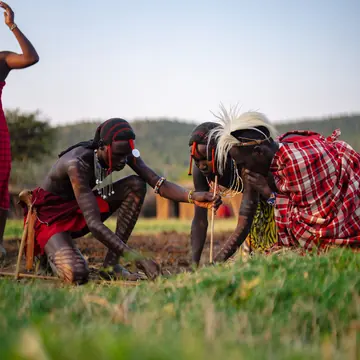 Maasai hosts in red shukas crouched together in the grass on the SYB Kenya trip